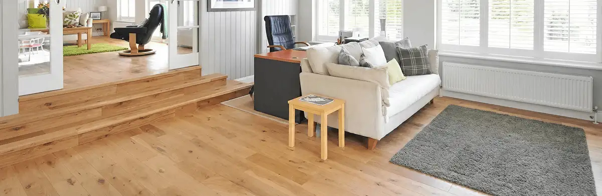 A modern living room with professionally installed laminate flooring, a beige sofa, a small side table, a gray rug, and large windows with white shutters in Albany, NY